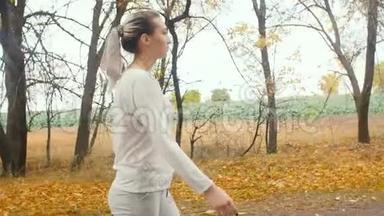 美丽的女孩穿着运动服装从事户外运动，女人走在柏油路上，开始沿着秋天的自然奔跑，